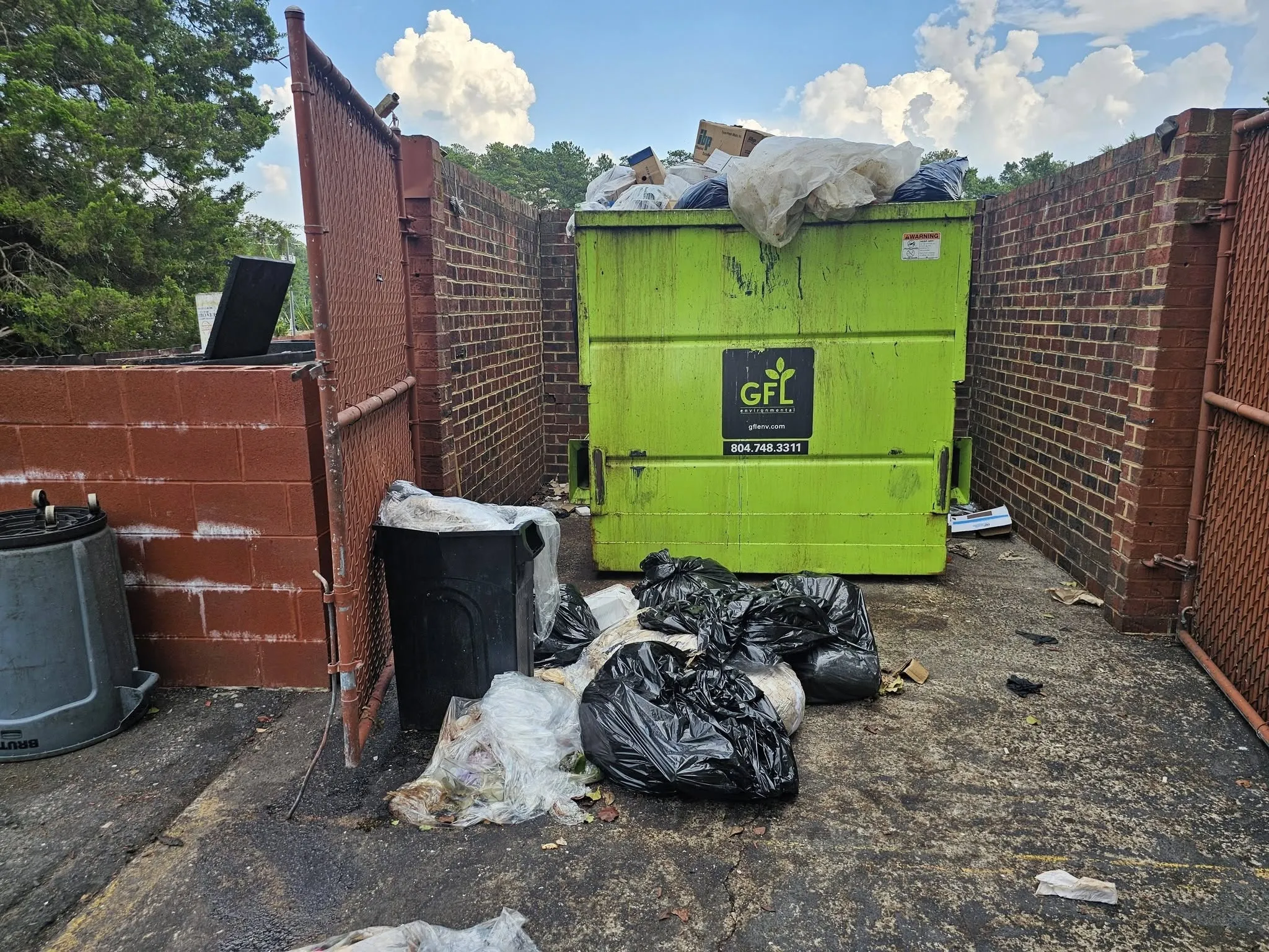 Dumpster corral overflowing with bagged trash and loose debris