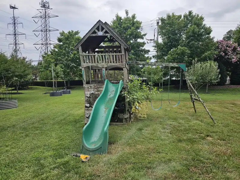 A wooden playset with a tower and slide on an open lawn in Glen Allen